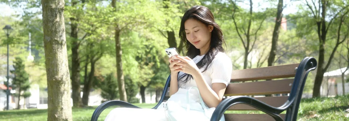 공원 벤치에서 여유롭게 휴대전화를 보는 모습